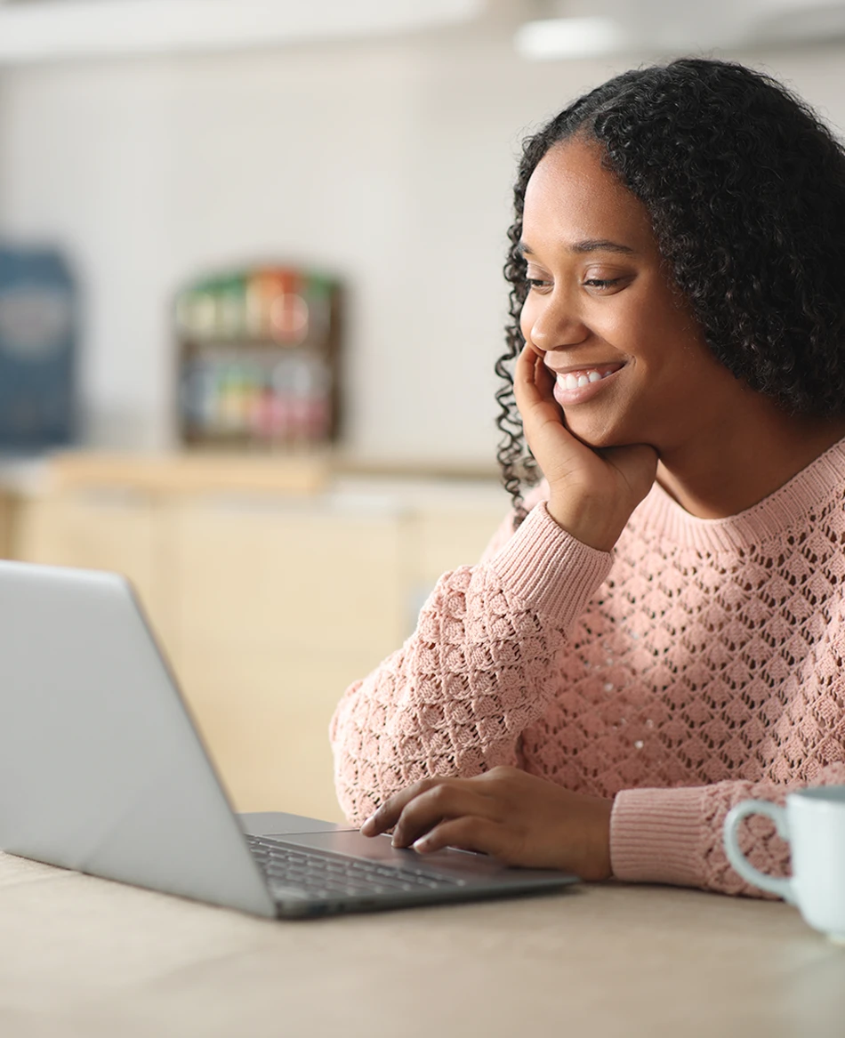A smiling woman rests her chin on her hand while using her laptop
