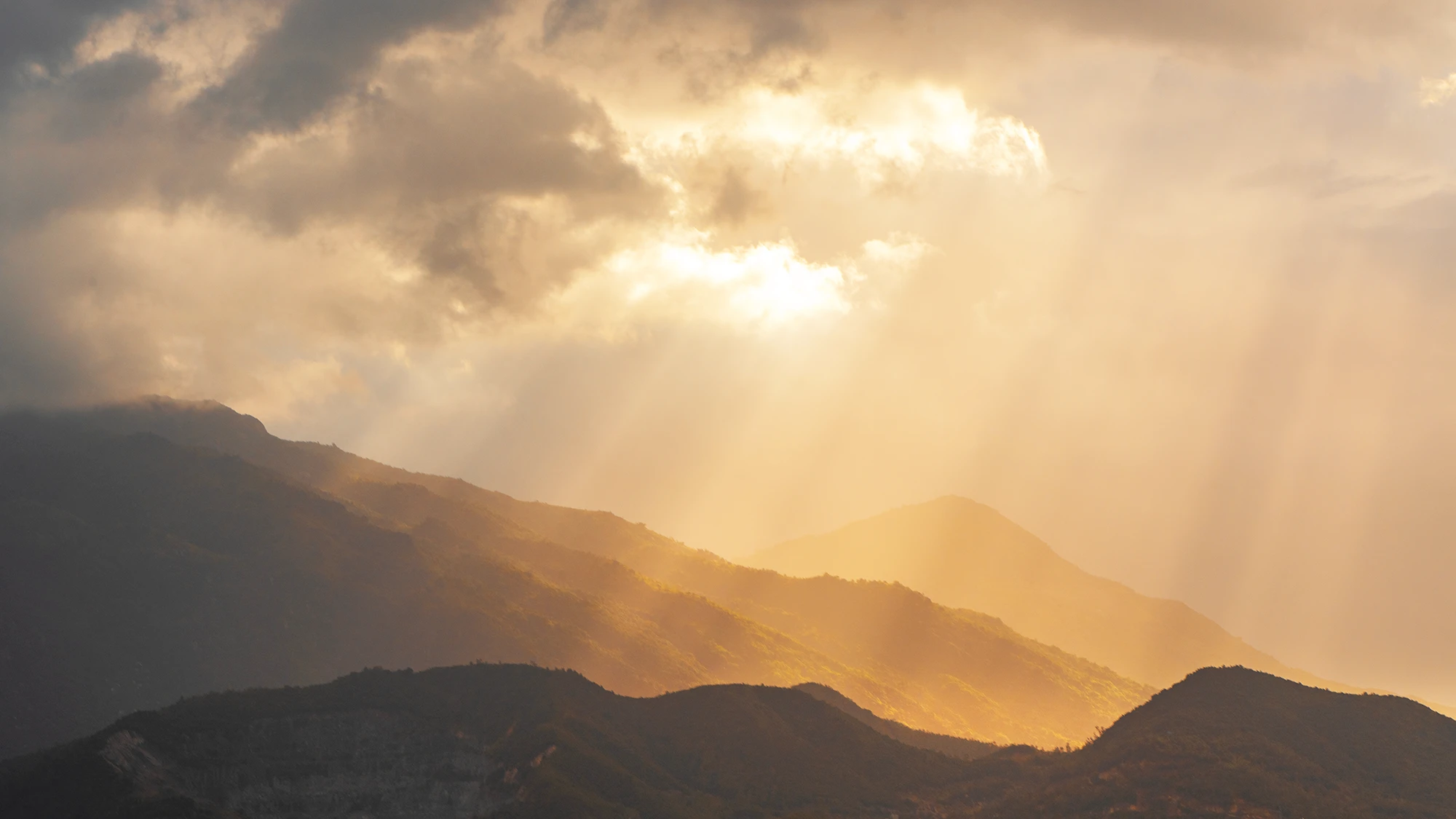 Golden light breaking through clouds over layered mountain ridges