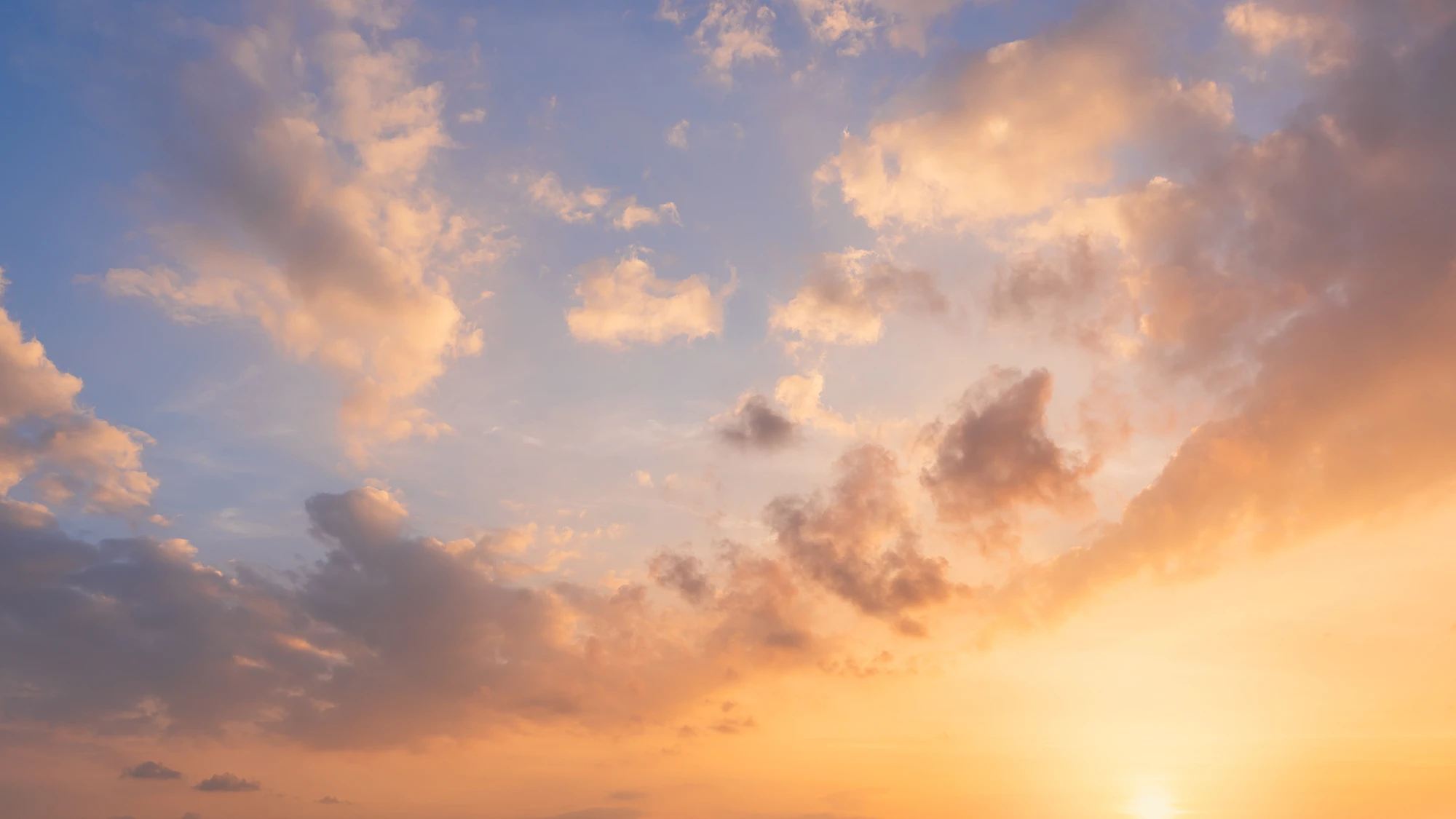 Soft clouds across a blue sky glowing orange and gold at sunset